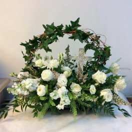 White floral arrangement with a decorative cross and ivy arch
