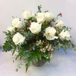 White roses arranged in a glass vase with mixed greenery and small accent flowers.