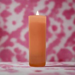 Lit orange pillar candle against a pink patterned background