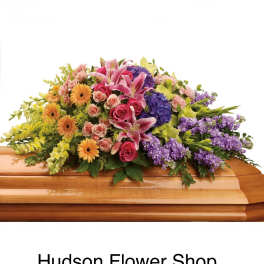 Colorful floral casket spray with pink lilies, roses, gerberas, and purple blooms