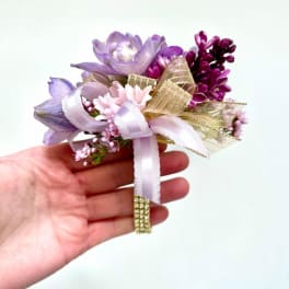 Small handheld corsage of purple and pink flowers with gold and lavender ribbon accents