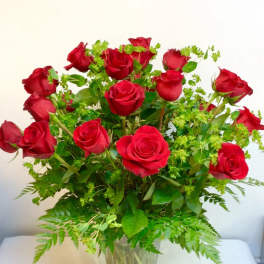 Red roses arranged in a clear glass vase with green filler