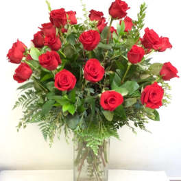 Red roses arranged in a clear glass vase with greenery