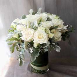 White roses arranged in a glass vase with silvery foliage