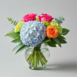 Bouquet of pink and orange roses with blue hydrangea in a glass vase