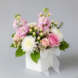 Pink and white flower arrangement in a white box with a ribbon