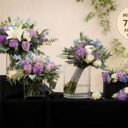Wedding floral set with purple, white, and blue blooms in glass vases, a bouquet, and a floral crown on black cloth