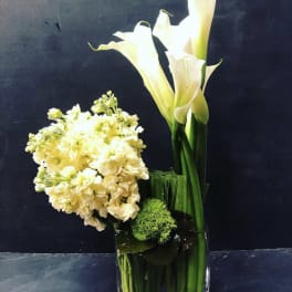 White calla lilies and pale yellow flowers in a glass vase