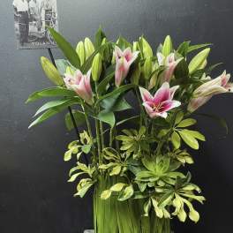 Pink and white lilies arranged with variegated greenery in a tall vase