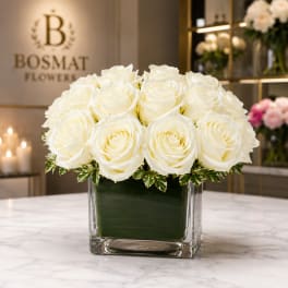 White roses arranged in a square glass vase with variegated foliage
