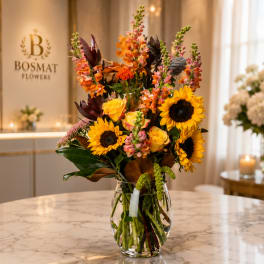 Tall bouquet of sunflowers, roses, and snapdragons in a clear glass vase