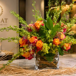 Bright orange and pink rose arrangement in a clear square vase