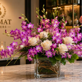 Purple orchids and white roses arranged in a clear glass vase