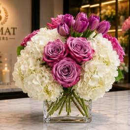 Pink roses and purple tulips in a clear glass vase with white hydrangeas