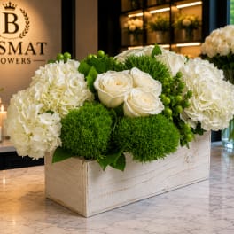 White roses and hydrangeas arranged in a wooden box with green accents.