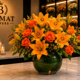 Orange lilies and roses arranged in a round glass vase