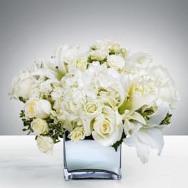 Low white arrangement of roses, hydrangeas, and lilies in a square glass vase