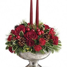 Red rose centerpiece with two burgundy taper candles in a silver pedestal bowl
