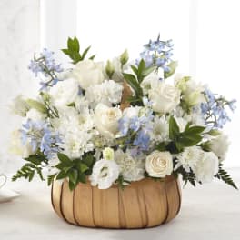 White and pale blue flower arrangement in a wooden basket