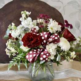 Red and white flower arrangement in a glass vase with a polka-dot ribbon