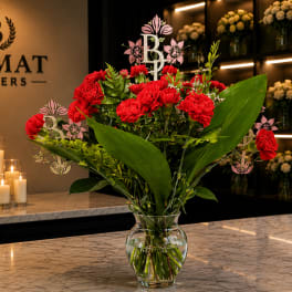 Red carnations in a clear glass vase with broad green leaves