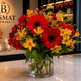 Red gerbera daisies and yellow alstroemeria in a clear glass vase