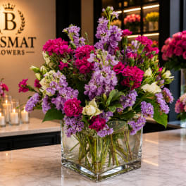Mixed pink and lavender flowers arranged in a clear square glass vase