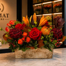 Mixed floral arrangement with red roses, orange lilies, and dark burgundy blooms in a rectangular vase