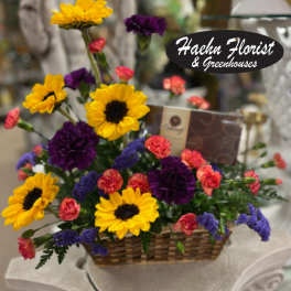 Basket arrangement with yellow sunflowers, purple carnations, and pink spray carnations