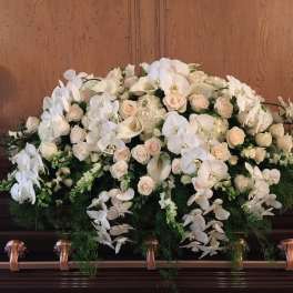 White floral casket spray with orchids, roses, and calla lilies