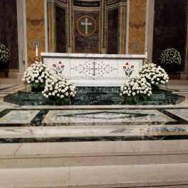 White floral arrangements on a church altar with a cross backdrop