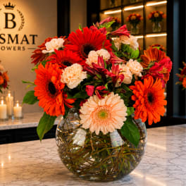 Bright mixed bouquet of gerbera daisies and carnations in a round glass vase