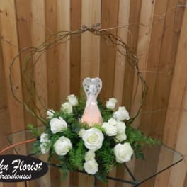 White roses arranged around a small angel figurine in a circular twig frame