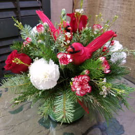 Holiday arrangement with red cardinals, roses, and white carnations in a green vase