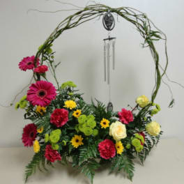 Floral arrangement with pink gerberas, roses, and yellow daisies in a circular vine frame