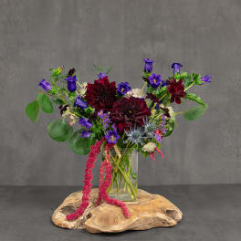 Purple and burgundy flowers in a clear glass vase on a wood slab