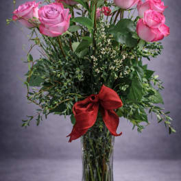 Pink roses in a clear glass vase with a red ribbon
