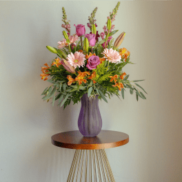 Mixed pink and orange flower arrangement in a purple vase