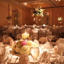 Floral centerpieces on round banquet tables in a warmly lit ballroom