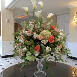 Large floral arrangement with white calla lilies and pink and coral roses in a glass vase