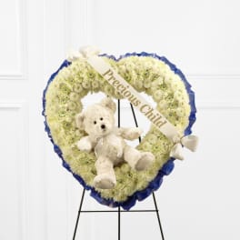 Heart-shaped white flower wreath with a teddy bear and ribbon on an easel