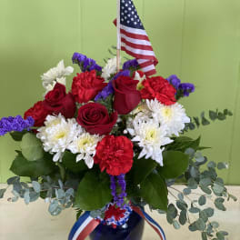 Red roses, white daisies, and carnations in a vase with an American flag