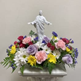 Mixed floral arrangement with a white religious statue centerpiece