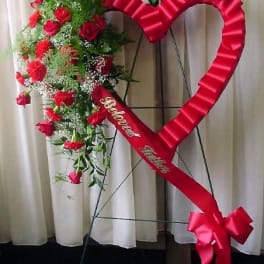 Heart-shaped floral standing spray with red roses and a red ribbon bow