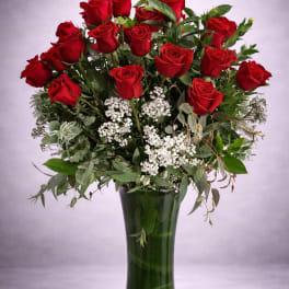 Red roses arranged in a tall glass vase with white filler flowers
