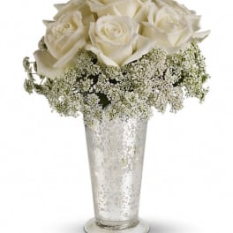 White roses in a tall silver vase with baby's breath