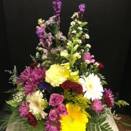 Tall mixed flower arrangement with daisies, roses, and lilies in bright colors