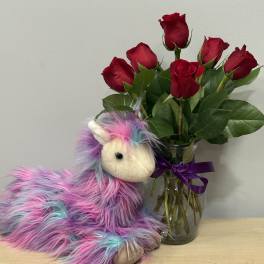 Red roses in a glass vase beside a colorful plush unicorn
