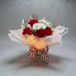 Red roses and white daisies in a wrapped bouquet with a heart-patterned bow