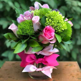 Pink roses and green blooms arranged in a glass vase with ribbon bows